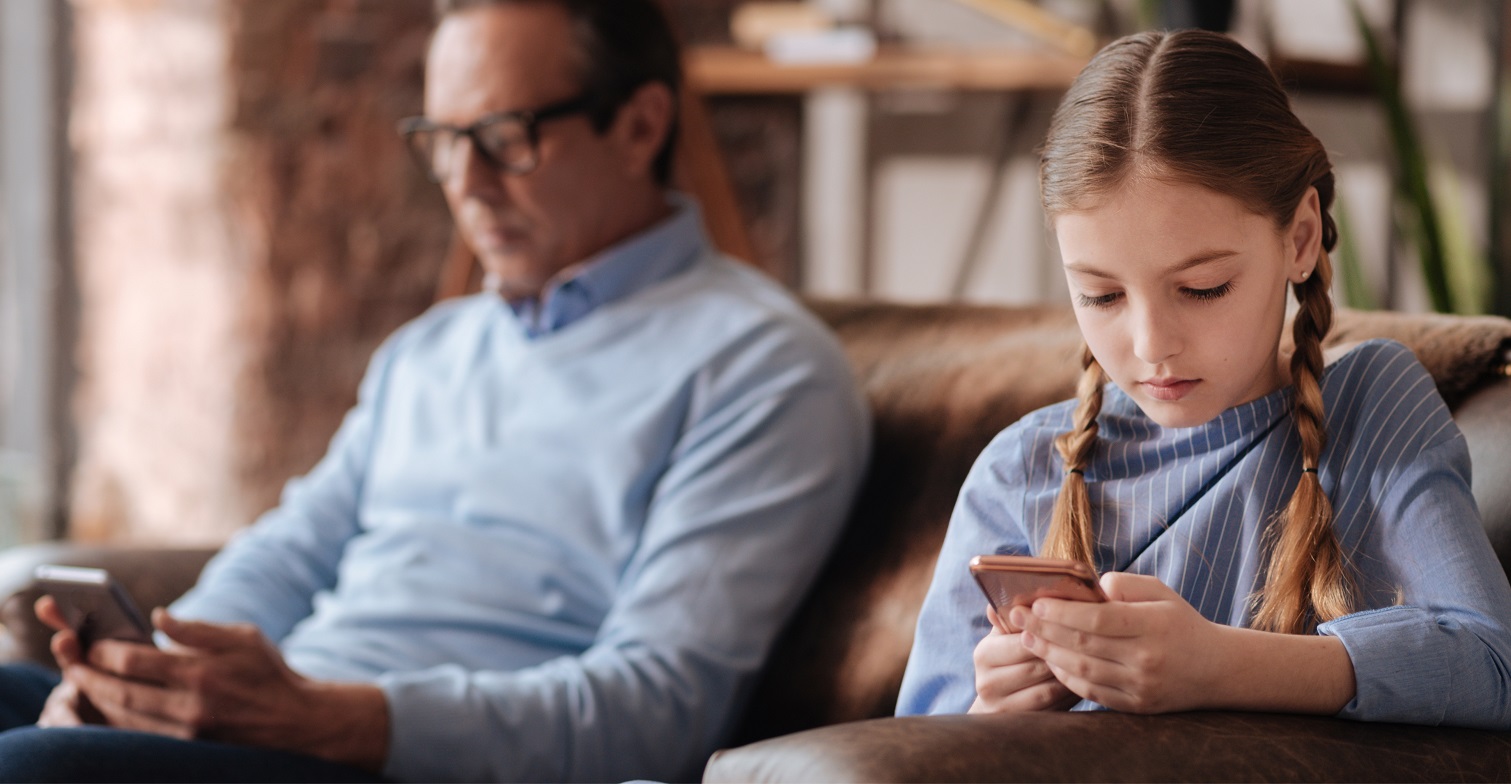 Themenschwerpunkt IT-Sicherheit: Sicheres Surfen im Internet für Kinder und Jugendliche. Zu sehen ist ein erwachsener mann und ein Kind auf einem Sofa. Beide bedienen ein Smartphone